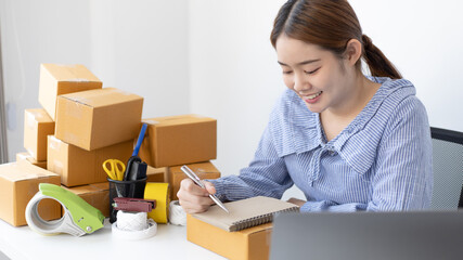 Young Asian woman is writing down the customer's details and addresses on the notebook in order to prepare for shipping according to the information, New kind of business for young, Sell online.