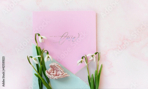 Do all things with love. notepad, snowdrops flowers, sleeping angel on pink background. inspiration, motivation image. spring season. Mother's day, Valentine's day, birthday concept. flat lay
