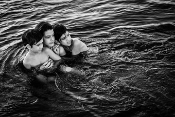 Três crianças abraçadas tomando banho de rio.