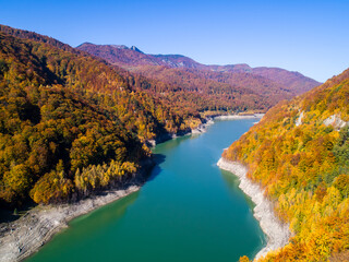 Aerial view of colorful forest trees and turquoise lake in the autumn season. Blue Lake and Autumn Forest Landscape Travel Concept. Fall forest and lake with colorful trees from above. October. 