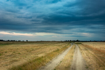 Country road through the fields and dark evening clouds