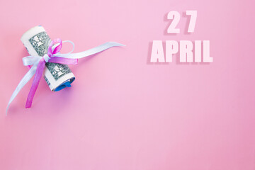 calendar date on pink background with rolled up dollar bills pinned by pink and blue ribbon with copy space. April 27 is the twenty-seventh day of the month