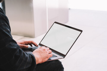 Unrecognizable man typing on keyboard of laptop with blank screen