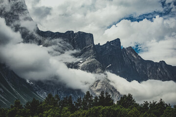 Massive dolomite cliff piercing trough clouds over forest in Norway 