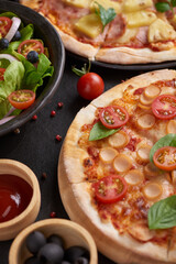 assorted foodset on table. Italian pizza and pizza cooking ingredients on dark stone background. tomatoes on vine, mozzarella, black olives, herbs and spices, vegetable salad. top view.