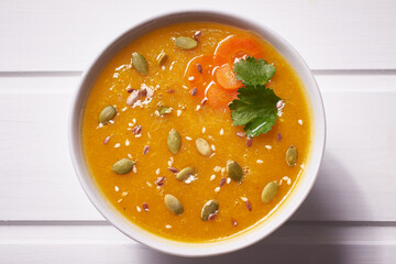 Pumpkin soup-puree with curry seasoning, whole grains and sesame seeds. Vegan Indian food on a white wooden table.