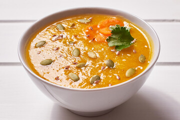 Pumpkin soup-puree with curry seasoning, whole grains and sesame seeds. Vegan Indian food on a white wooden table.