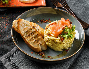 Delicious breakfast with scrambled eggs with salmon on top, salad, and toast on plate over dark background. Healthy breakfast concept, close up