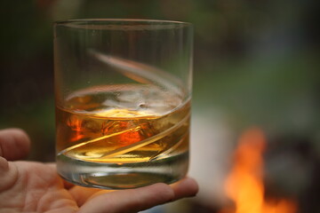 Hand holding full whiskey glass at fireplace