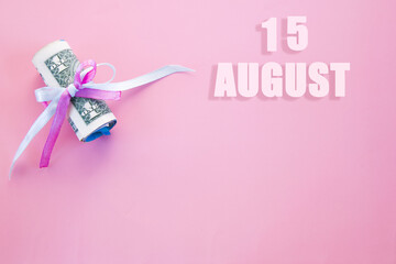 calendar date on pink background with rolled up dollar bills pinned by pink and blue ribbon with copy space. August 15 is the fifteenth day of the month