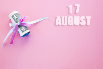 calendar date on pink background with rolled up dollar bills pinned by pink and blue ribbon with copy space.  August 17 is the seventeenth day of the month