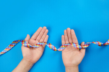 World Autism awareness day. Autistic boy hands holding puzzle pattern ribbon on blue background