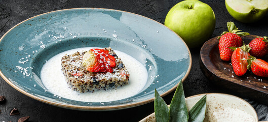 Quinoa porridge with fruits, strawberries, blueberry, pineapple and coconut milk in bowl over dark background with. Healthy vegan food, clean eating, dieting, top view