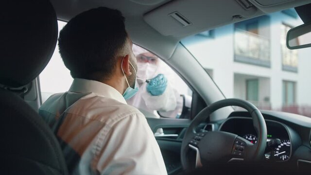 Nurse performing swab test on the man in the drivers seat. Mobile covid testing station. High quality 4k footage