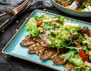 Summer salad with steak, green leaves, arugula, corn, apple, and tomato on a dark background, close up view. Healthy food, clean eating, dieting