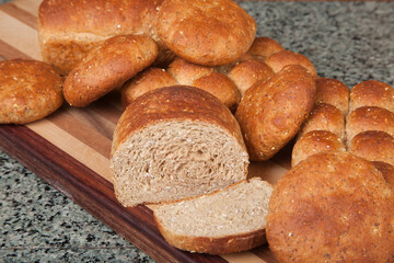 Multigrain rolls, buns and loaf with a slice cut off, on bread board.