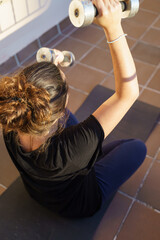 Caucasian woman doing sport on the terrace of her house with weights and a mat. Palma de Mallorca, Spain