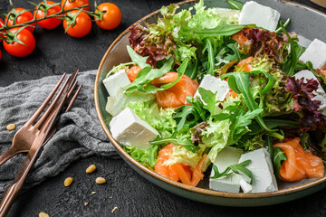 Fresh Salmon salad with fish, spinach, basil, arugula, salad leaves, and feta cheese on bowl over dark background, close up view. Healthy food, clean eating, dieting