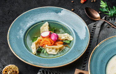 Delicious homemade chicken soup with dumpling and vegetables in plate on dark background, close up view. Traditional healthy food