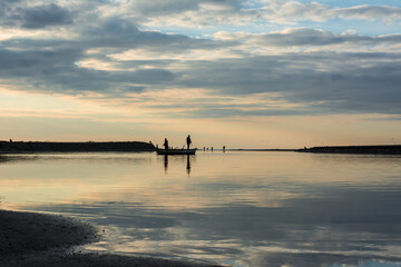Reflection of clouds and a fishing boat in the calm lake, Two people in the wooden boat catch fish...