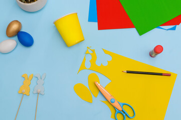 Happy Easter day.Festive craft from a paper cup with your own hands.Leisure for children.A congratulatory gift.Cute yellow Easter bunny on blue background