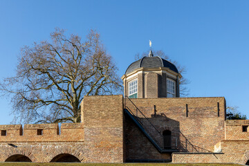 Obraz premium Part of the medieval protective city wall and tower of Bourgonjetoren sticking out with a tree in the background against a clear blue sky in historic Hanseatic town Zutphen in The Netherlands