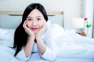 Portrait images of  Asian attractive woman Lie down and rest on the white bed, In her bedroom which happily, before wake up in the morning,  to people and stay at home concept