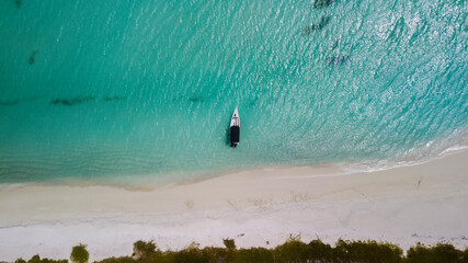 Top view photo of a beach with white sand and light blue, with some boats on it.
