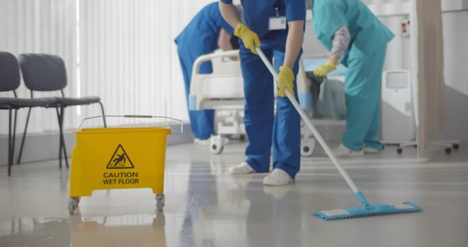 Nurses mopping floor and making bed in empty hospital ward