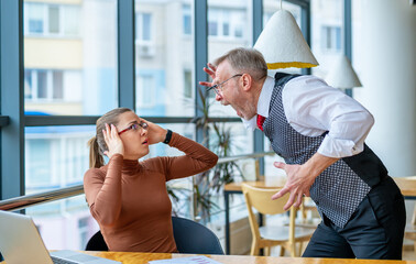 Angry businessman shouting on his woman collegue. Confused woman in glasess holding her hands near...