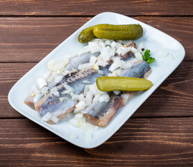 Herring fillet with chopped onions on a white plate and a wooden table.