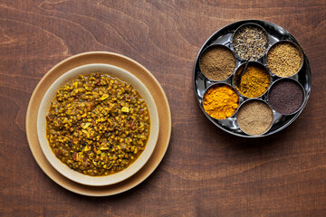 Whole mung bean curry and set of Indian cuisine spices in masala dabba spice box on brown wooden...