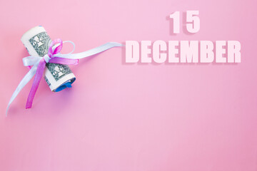 calendar date on pink background with rolled up dollar bills pinned by pink and blue ribbon with copy space. December 15 is the fifteenth day of the month