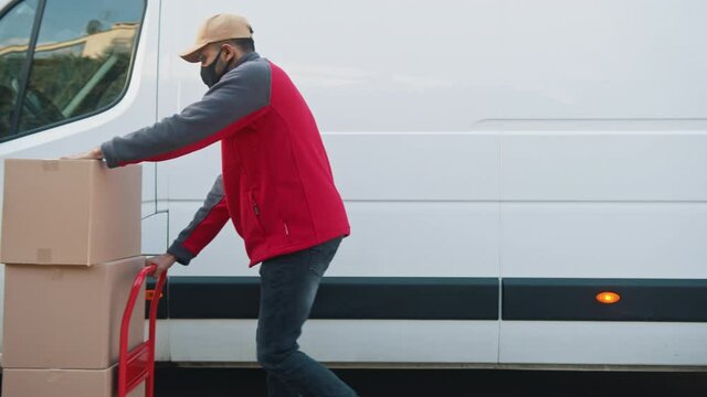 Man with face mask pushing cardboard boxes on the troley. Delivery of parcels during covid19 outbreak. High quality 4k footage