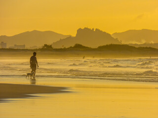Fototapeta na wymiar Siluetas de un hombre y su perro paseando por la playa de Somo, en la bahía de Santander, España, al atardecer