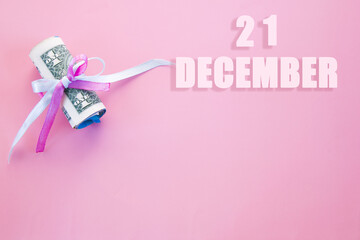 calendar date on pink background with rolled up dollar bills pinned by pink and blue ribbon with copy space. December 21 is the twenty first day of the month