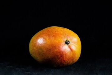 Fototapeta na wymiar Eine einzelne Mangofrucht reigestellt vor schwarzem Hintergrund - Das Bild ist gut geeignet als Hintergrundbild für Desktops und Monitore
