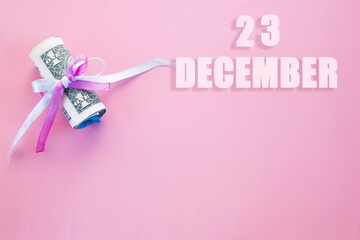 calendar date on pink background with rolled up dollar bills pinned by pink and blue ribbon with copy space. December 23 is the twenty-third  day of the month