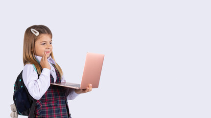 Banner- long format. Online lessons. An elementary school student in uniform with a laptop computer on a grey background with empty side space for text or advertising.