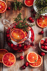 Citrus and berry tea with cranberries, blood oranges and thyme in a glass teapot on wooden table.