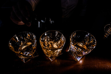 Top view of man pouring whiskey into glasses on the dark light background.