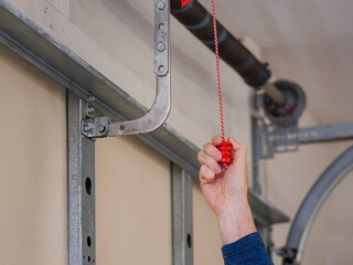 Man pulling manual safety release cord handle before performing maintenance on electric garage door opener.