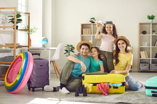 Portrait of happy family with children ready for summer vacation travel sitting on home living-room floor surrounded with packed clothes in travel suitcase bag. Holiday journey preparation