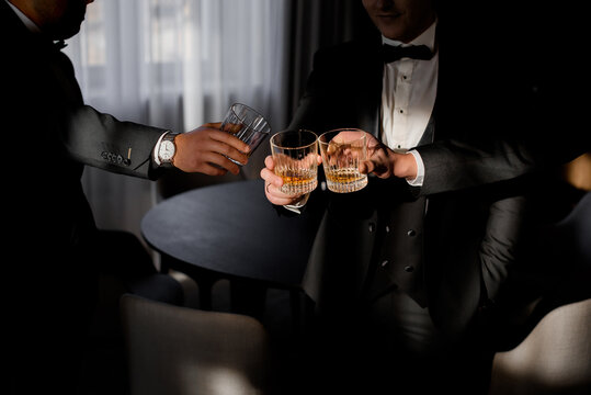 Front view of men dressed in business costumes drinking whiskey. Concept of luxury lifestyle.