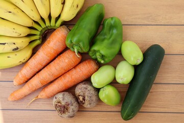 Fruits and vegetables on wooden background. Bananas, carrots, green tomatoes, cucumber, beets and bell pepper. Organics.