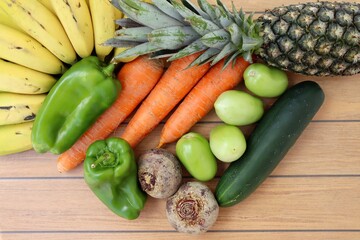 Fruits and vegetables on wooden background. Pineapple, bananas, carrots, green tomatoes, beets and bell pepper. Organics.