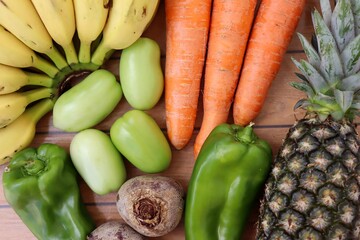 Fruits and vegetables on wooden background. Pineapple, bananas, carrots, green tomatoes, beets and bell pepper. Organics.
