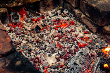 Glowing embers in hot red color, abstract background. The hot embers of burning wood log fire. Firewood burning on grill. Texture fire bonfire embers.