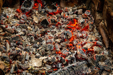 Glowing embers in hot red color, abstract background. The hot embers of burning wood log fire. Firewood burning on grill. Texture fire bonfire embers.