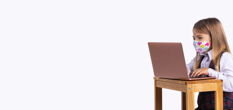 Banner,long format. Caucasian schoolgirl in uniform and a medical mask sits at a table with a laptop. The concept of training during covid 19. Preventing the spread of the virus.